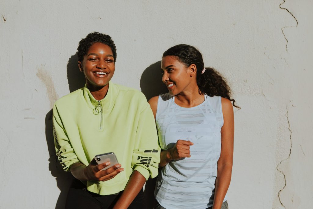 Two happy women holding phone in front of wall